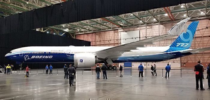 A Boeing 777X sitting in a hanger surrounded by employees.