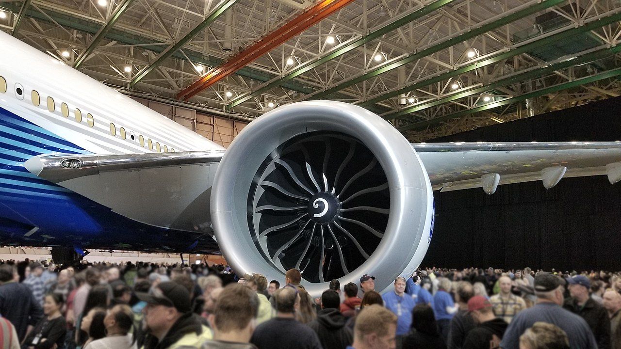 A Boeing 777X sitting in a hanger surrounded by people, focused in on the GE9X engine.