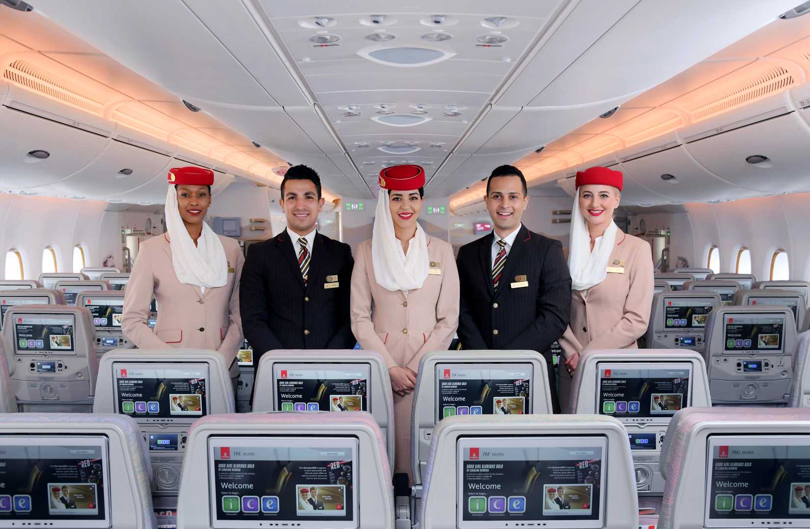 Five Emirates Cabin Crew members standing in the economy section of an aircraft.