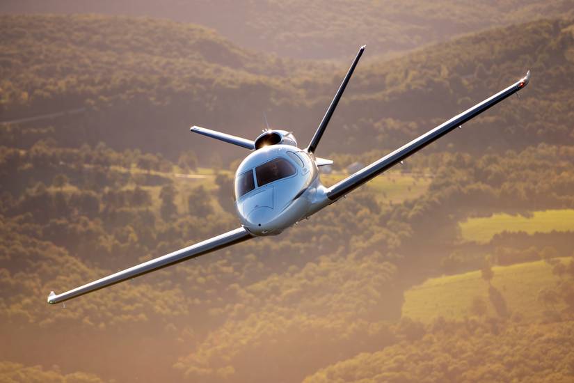 A Cirrus Vision Jet flying above grass and trees.