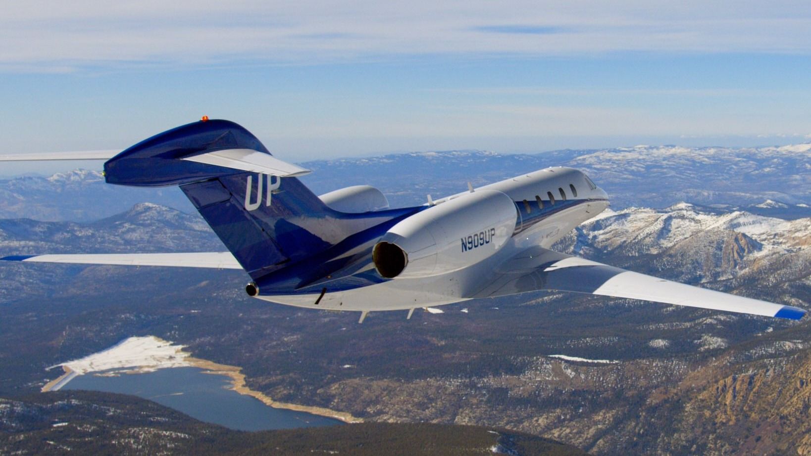A Wheels Up jet flying above mountainous terrain.