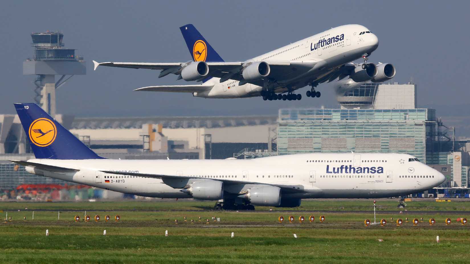 A Lufthansa Airbus A380 taking off with a taxiing Lufthansa Boeing 747 in the foreground.
