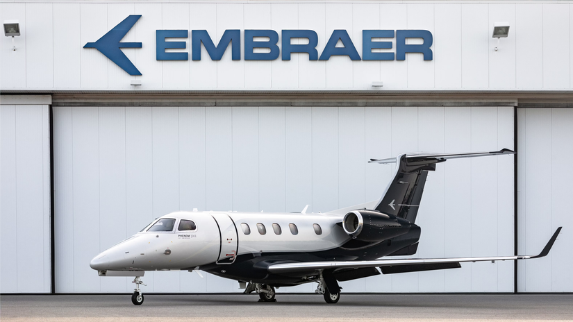 An Embraer Phenom 300E parked right outside of an aircraft hangar.