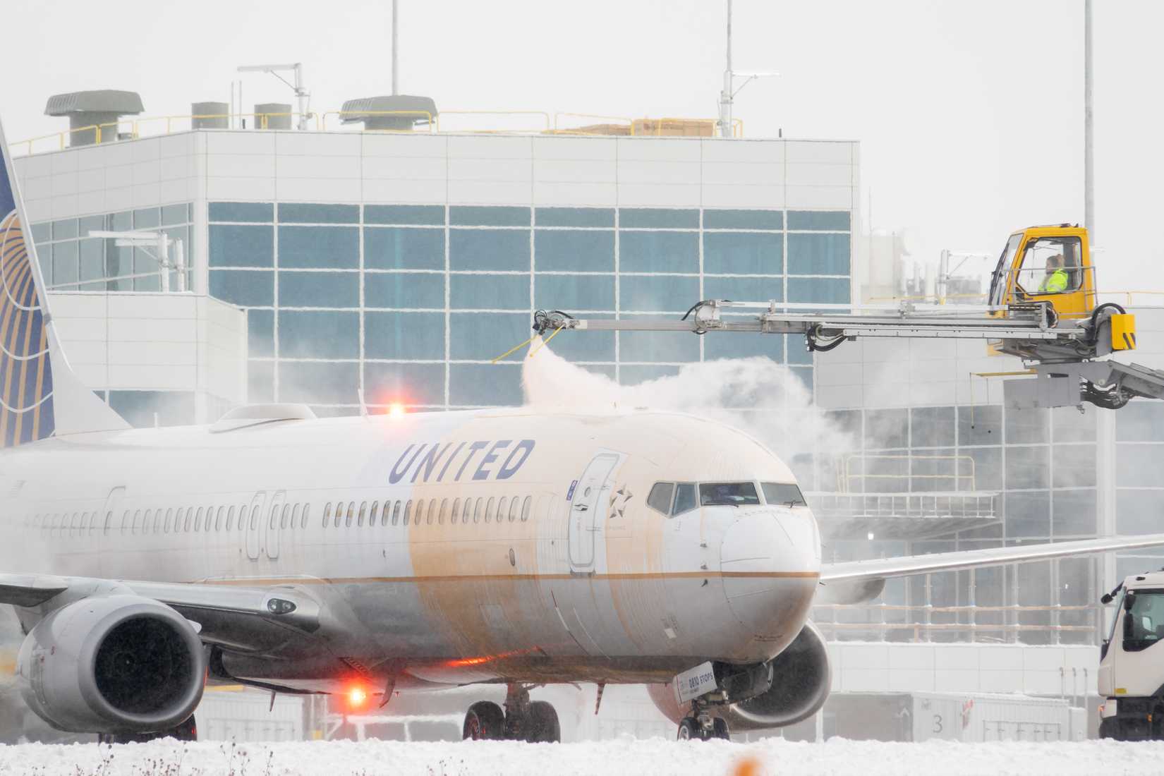 A United Airlines plane being de-iced on a snowy airport apron.