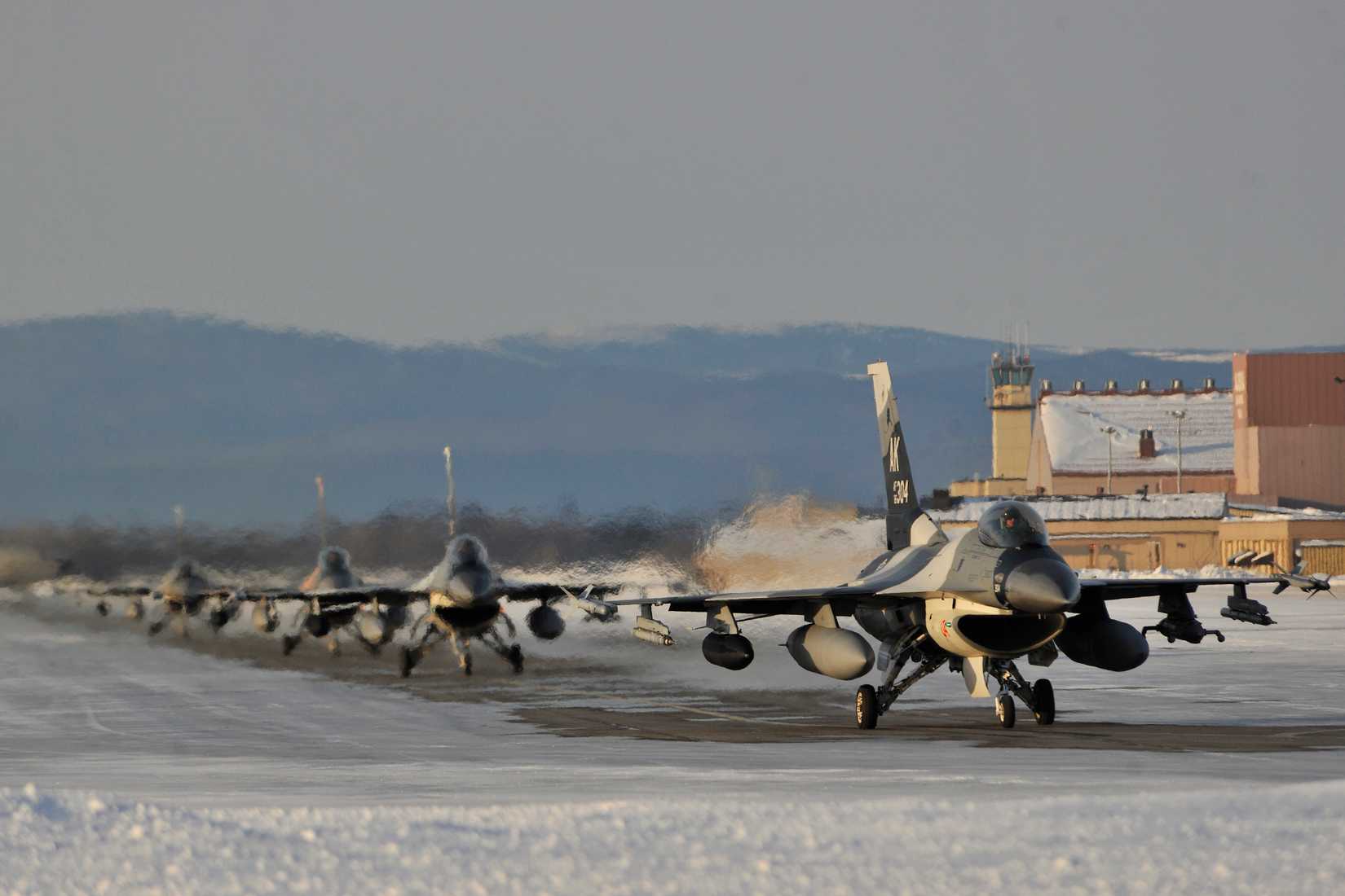 Several fighter jets lined up on a snowy airport apron.
