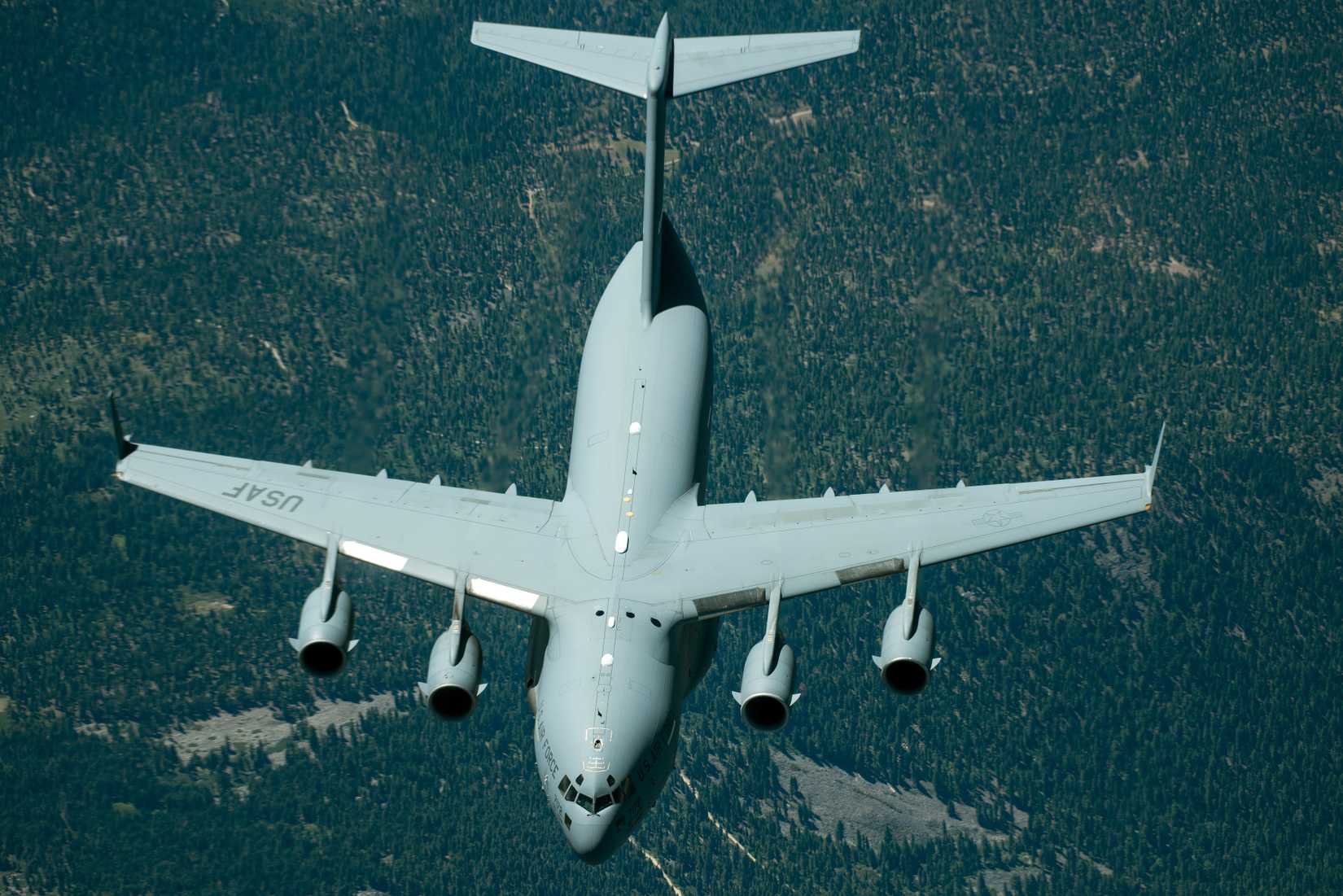 A C-17 Globemaster III flying over land, seen from above.