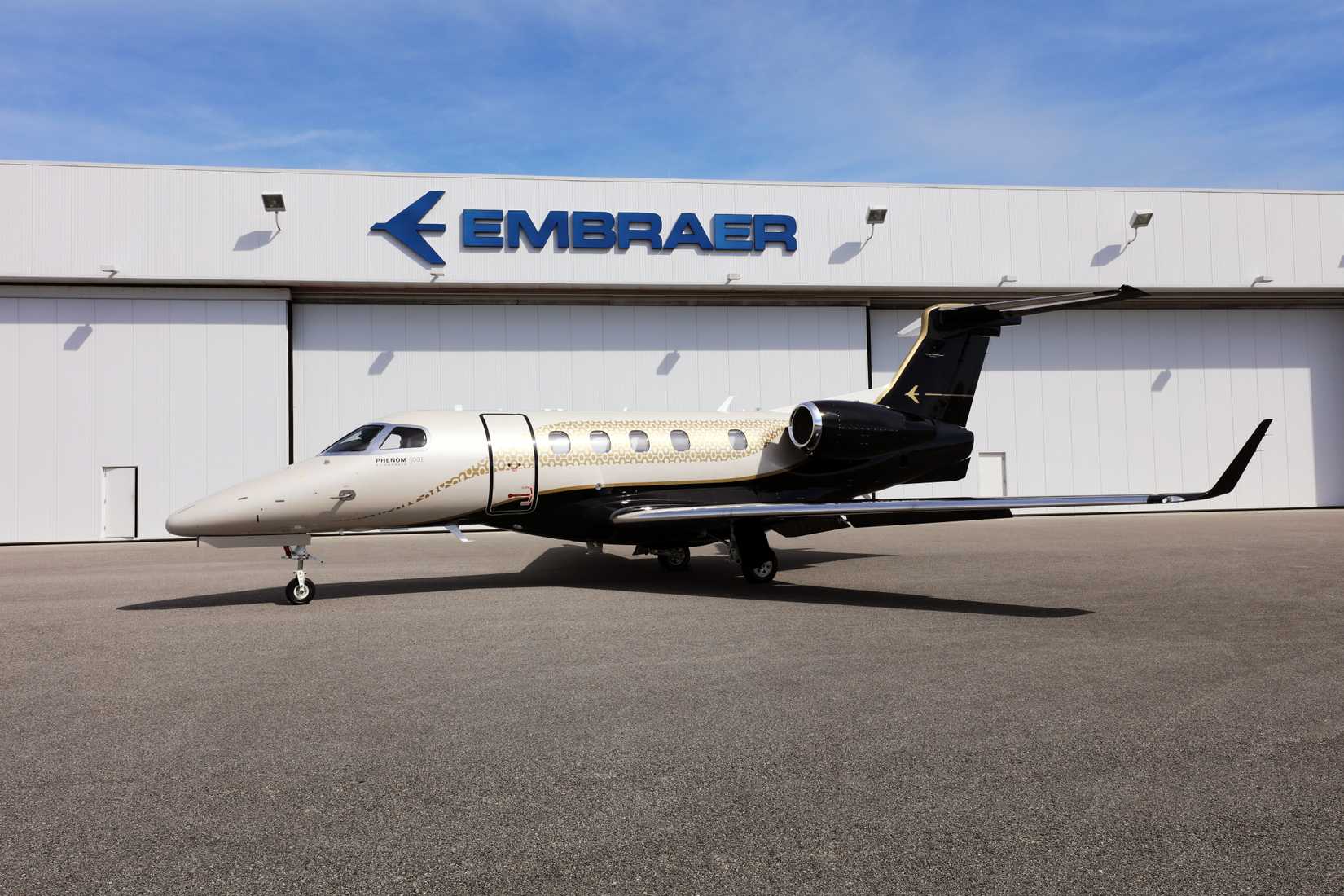 An Embraer Phenom 300E parked near a hangar.
