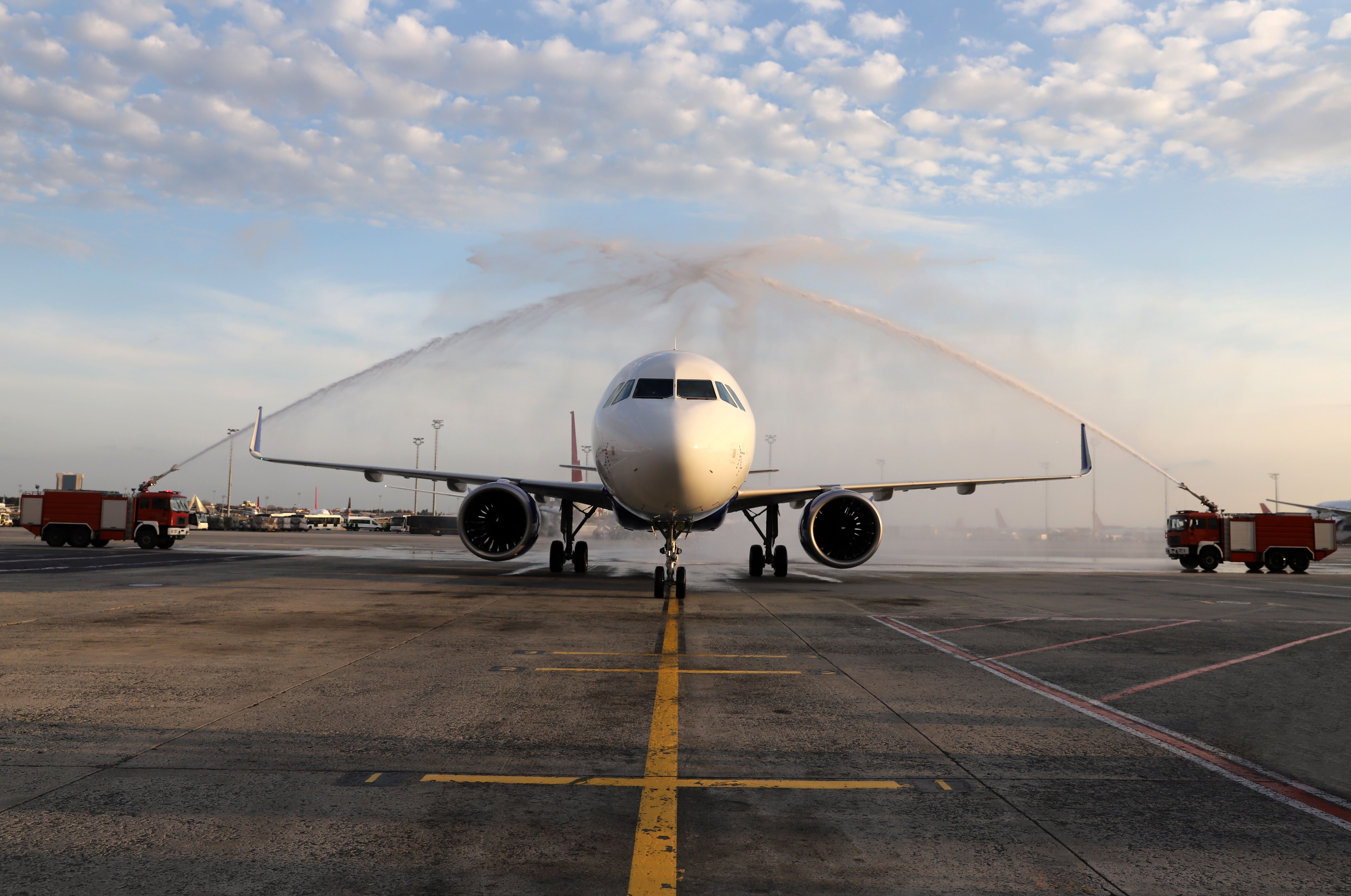 An aircraft underneath two streams of water coming from firetrucks on either side.
