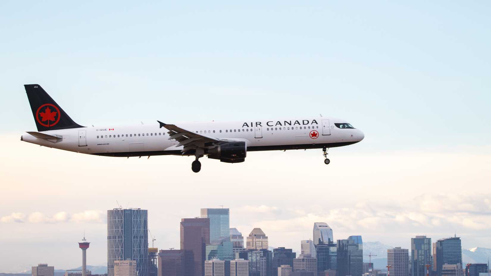 An Air Canada Airbus A321 flying in the sky with a city skyline in the background.