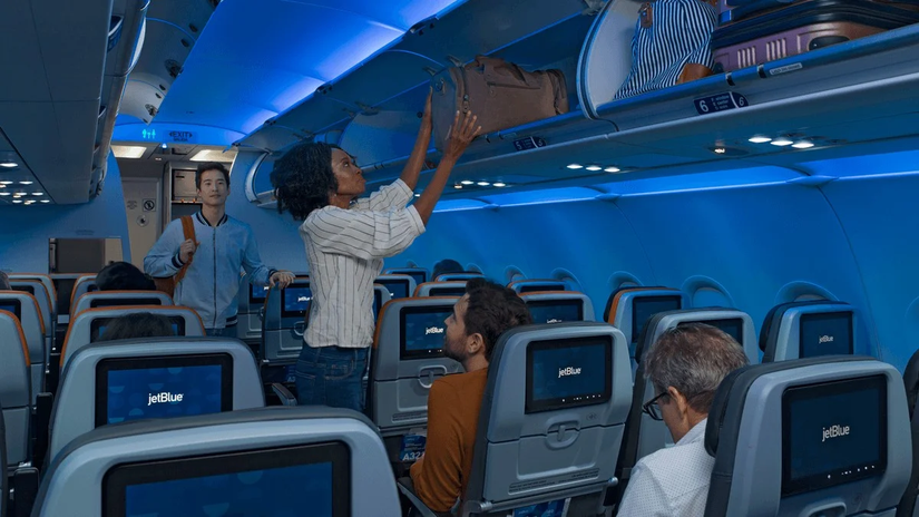 Passengers putting luggage into the Overhead Bins on a JetBlue aircraft.