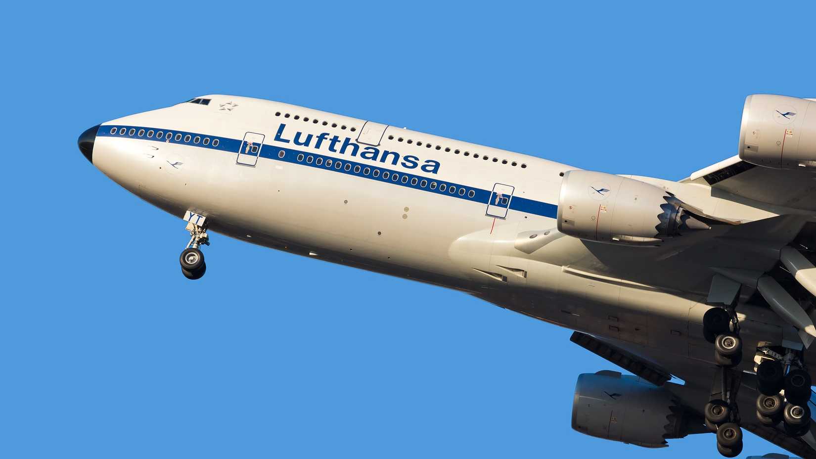 A closeup of the front half of a Lufthansa Boeing 747-8 with a retro livery flying in the sky.