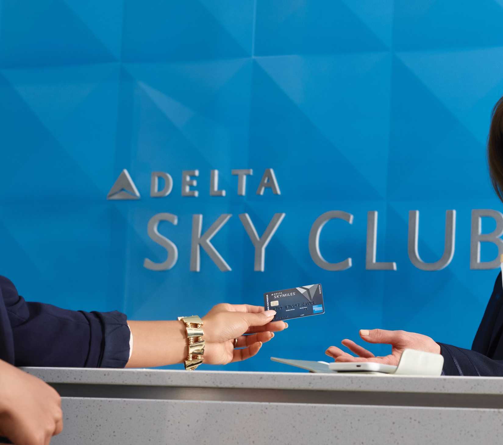 An individual handing a Delta Sky Club desk agent their Delta SkyMilees credit card.