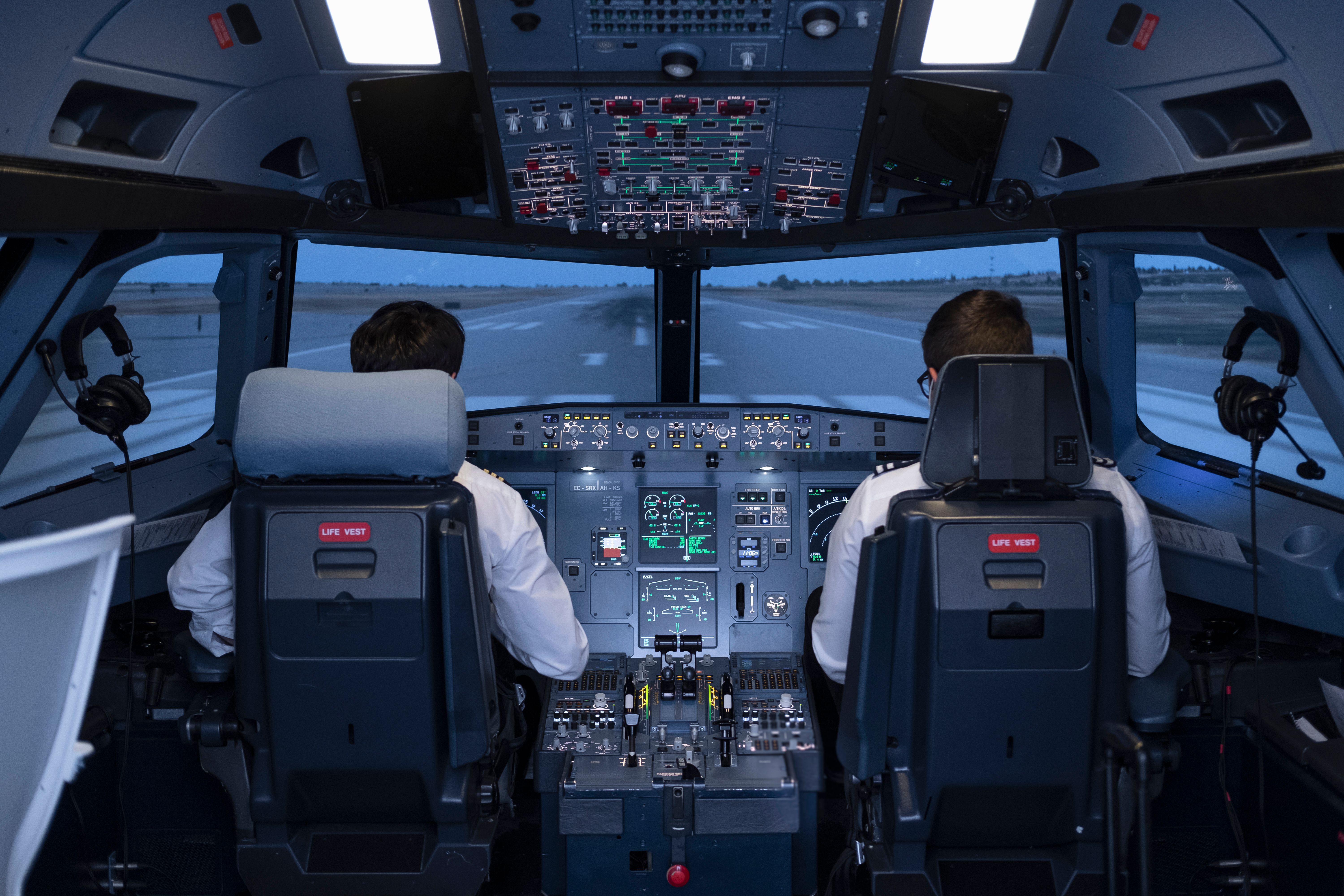 General view of the cockpit of a commercial flight simulator, with two pilots sitting in their seats preparing to start the flight during a flight practice