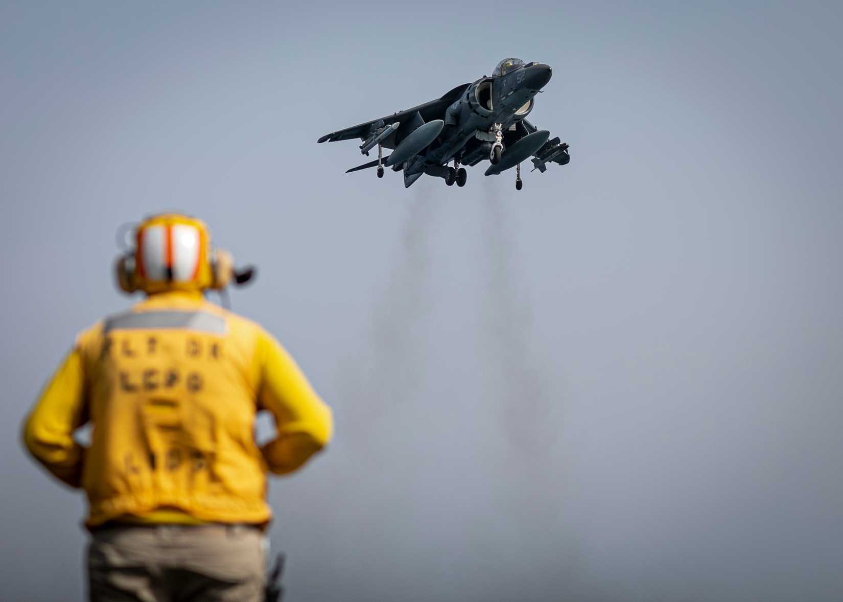 A Sailor assigned to amphibious assault ship USS Bataan (LHD 5) participates in flight operations with a U.S. Marine Corps AV-8B Harrier II aircraft, attached to Marine Medium Tiltrotor Squadron 162