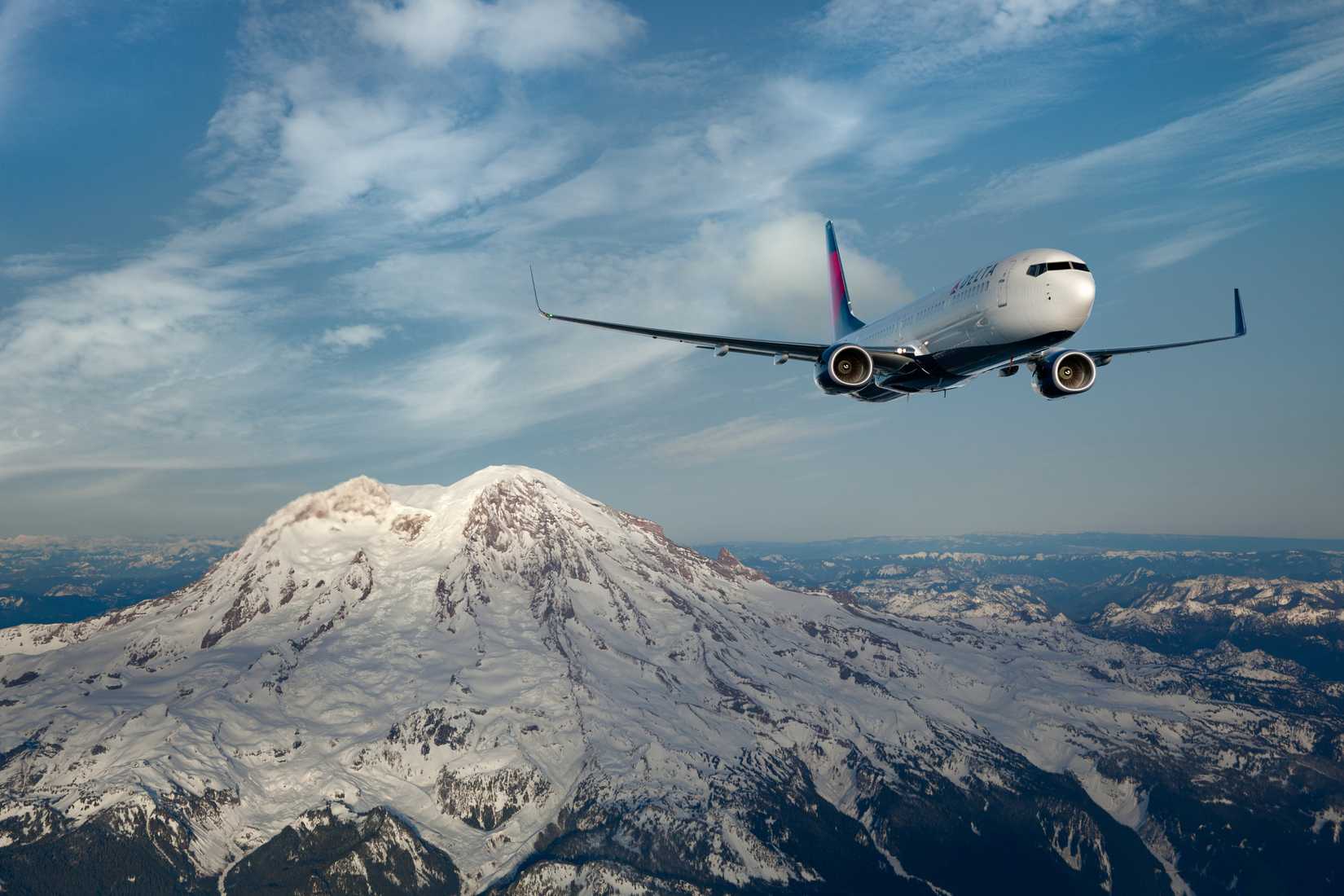 A 737-900 flies over snow-capped mountains.