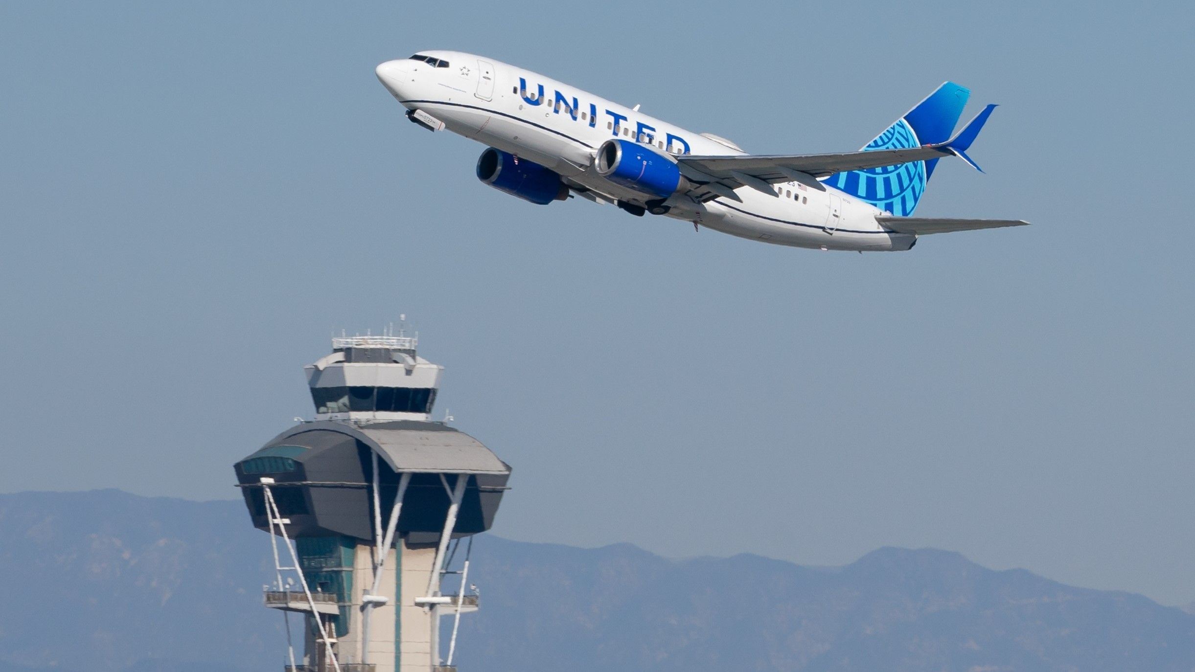A United Airlines Boeing 737-700 departing LAX with the control tower visible in the photo
