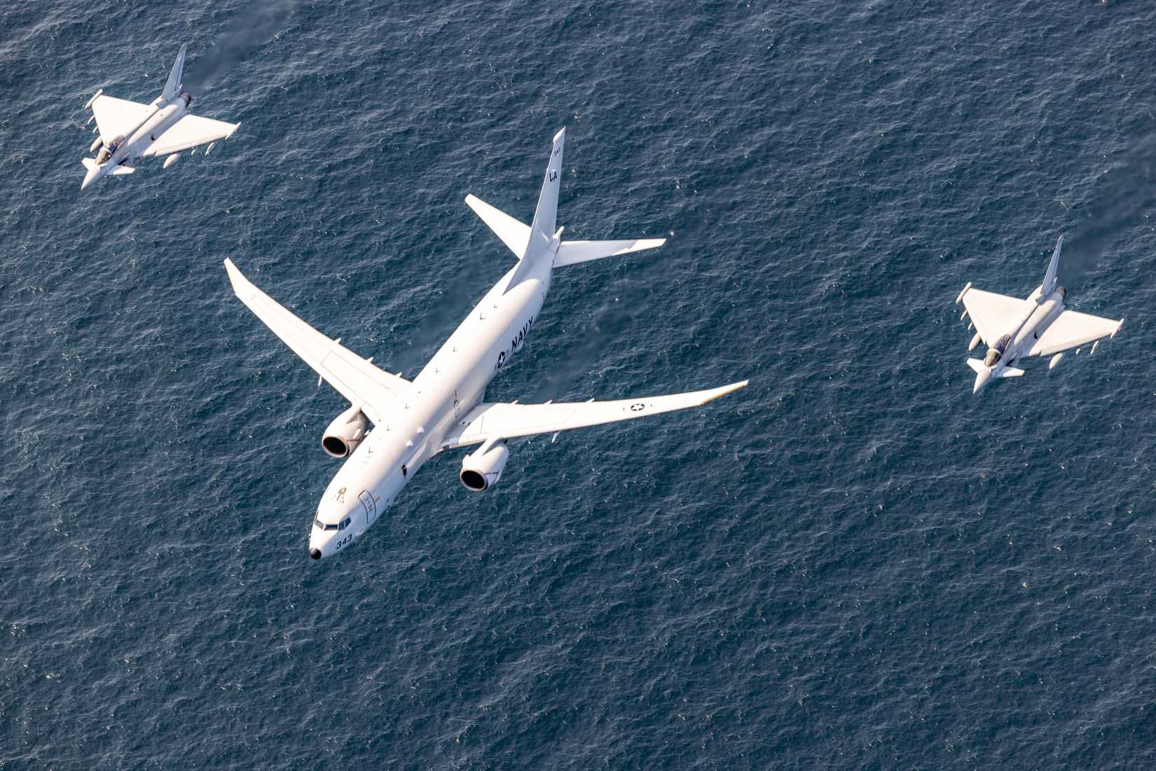 A U.S. Navy P-8A Poseidon, center, and two Royal Air Force Eurofighter Typhoon fighter aircraft participate in an aerial formation during exercise Baltic Operations 2025.