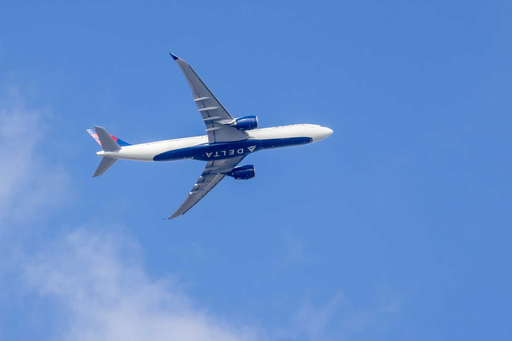 Delta air lines airbus a330 banking during a flight in a blue sky with some clouds