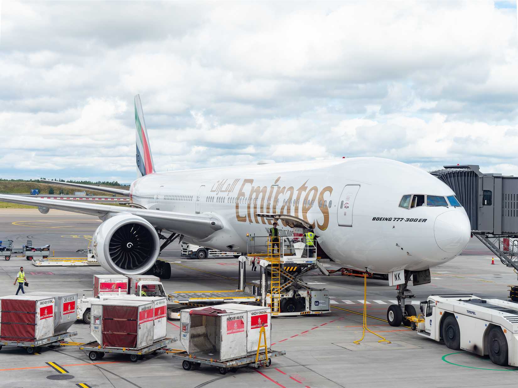 Emirates Boeing 777-300ER at a gate of Oslo Airport, Gardermoen, being loaded with cargo and luggage containers before departure.