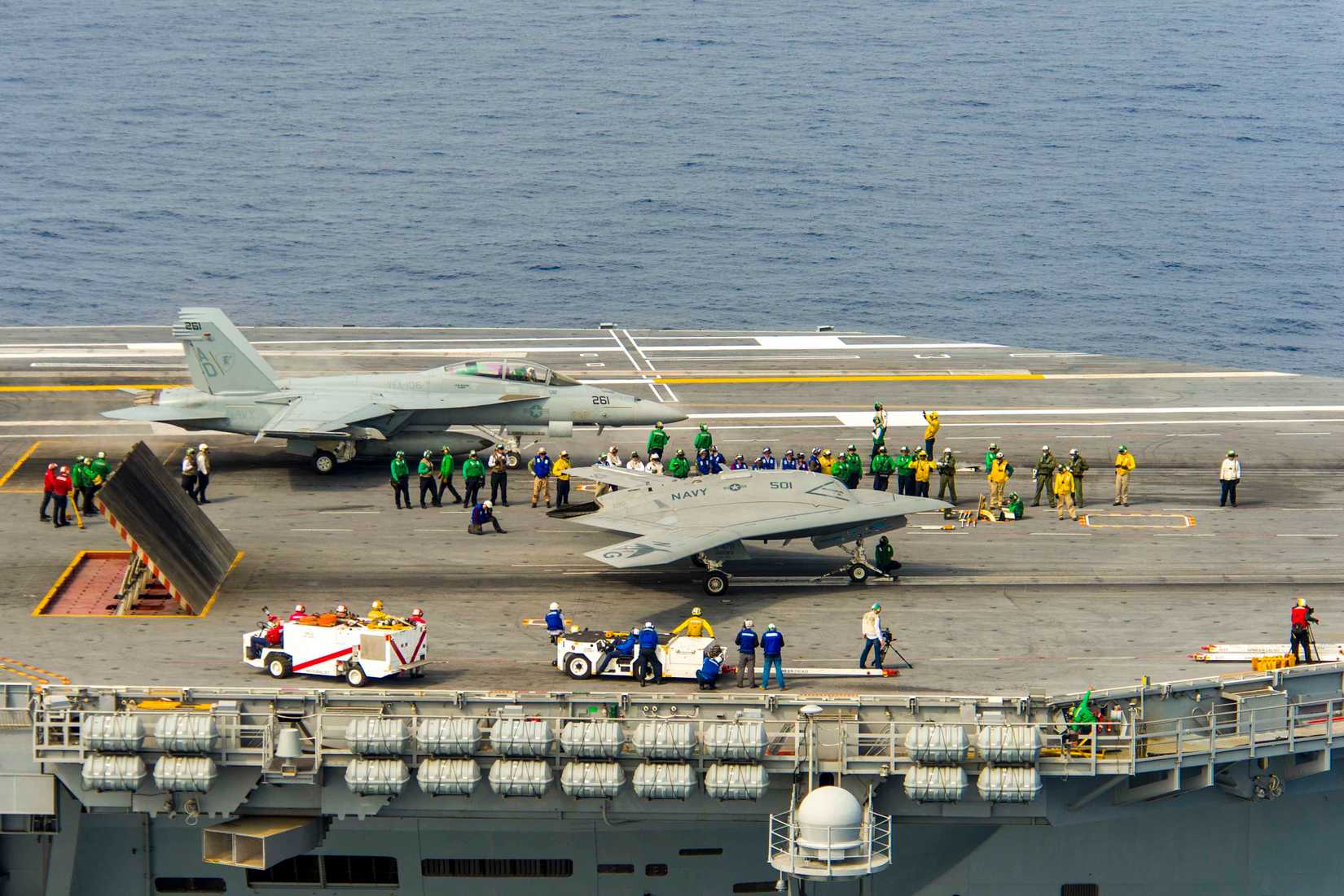 The Navy's unmanned X-47B, right, conducts flight operations aboard the aircraft carrier USS Theodore Roosevelt (CVN 71).