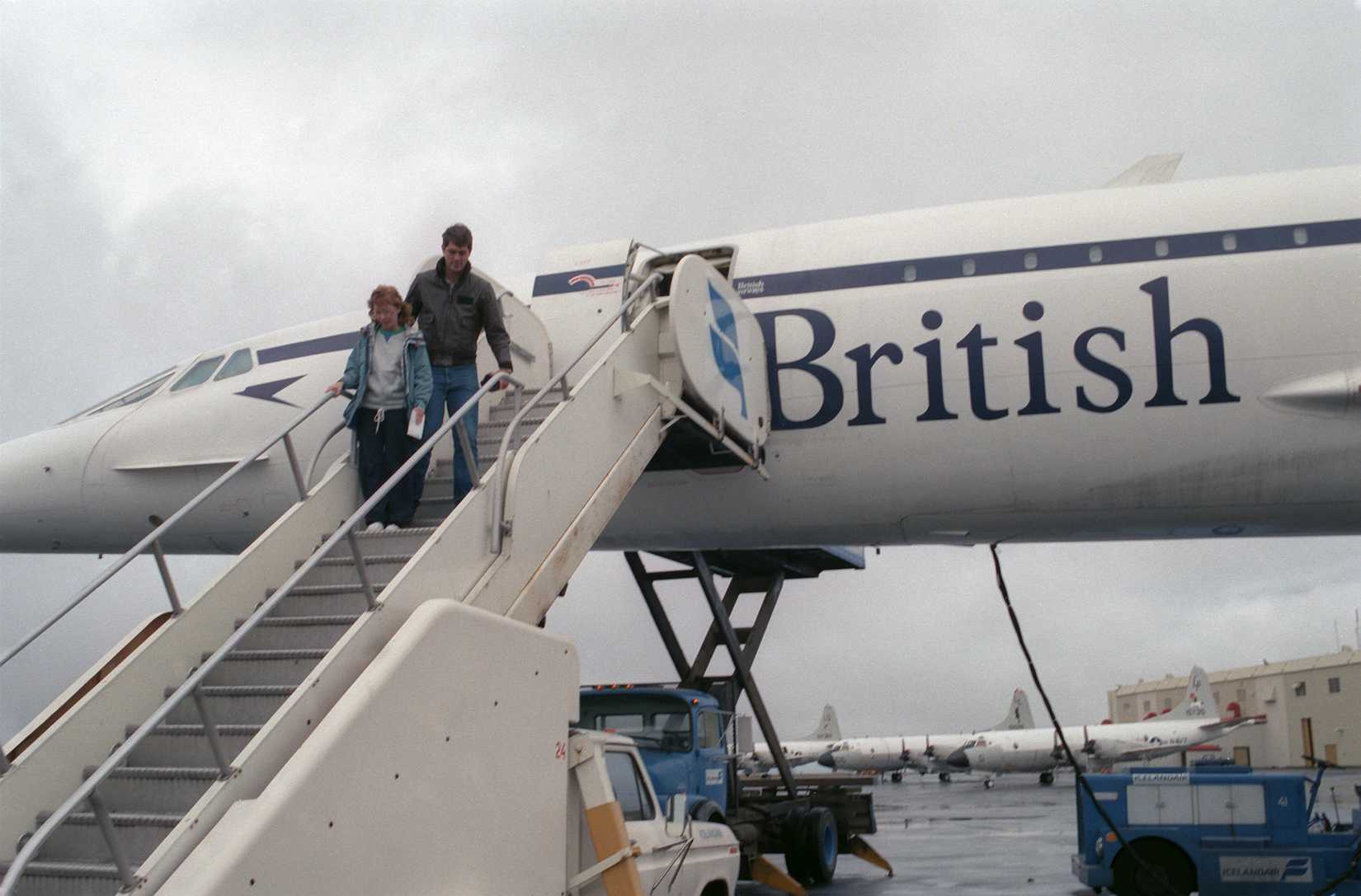 Two passengers exit a British Airways Concorde aircraft parked on the flight line. The aircraft is on an around-the-world test flight.