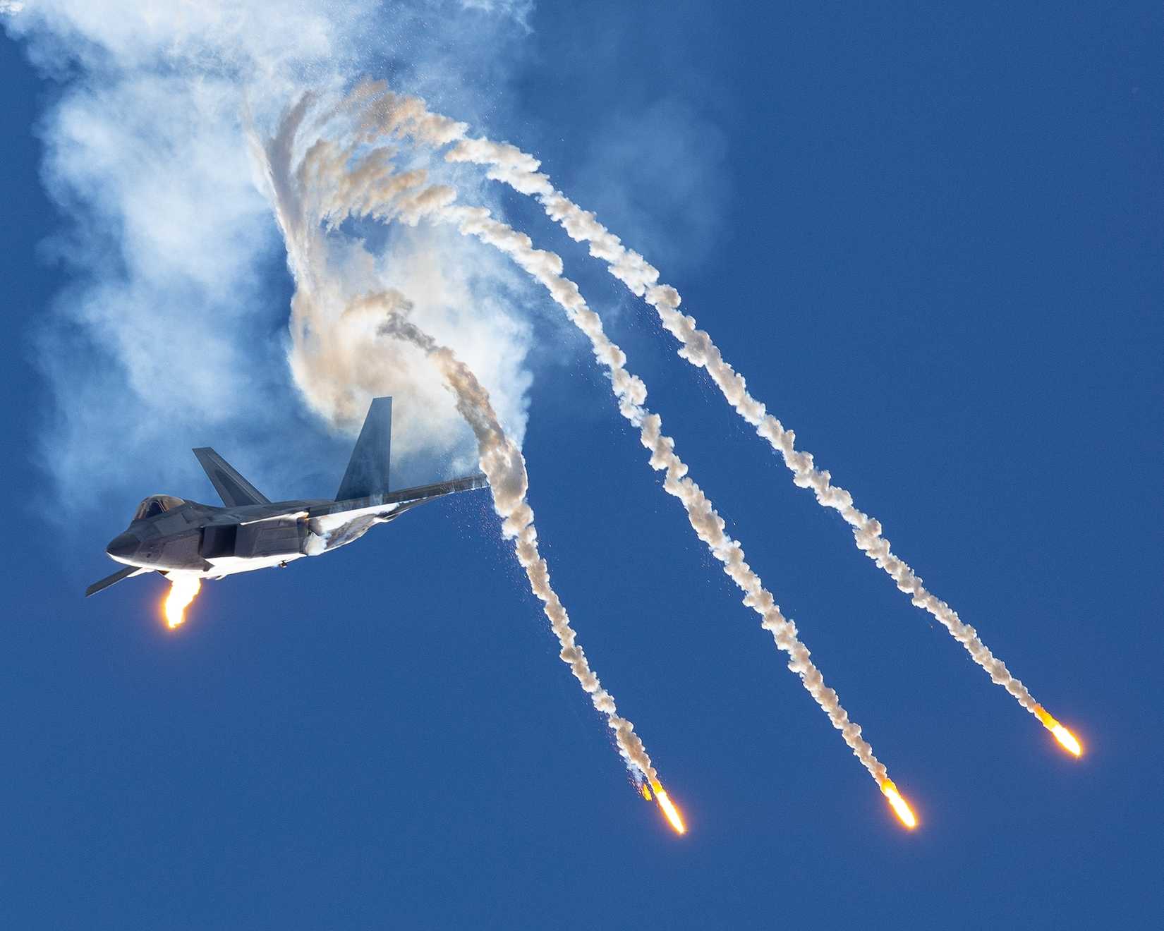 Epic frontal view of a F-22 Raptor deploying flares in a turn, in smoke.