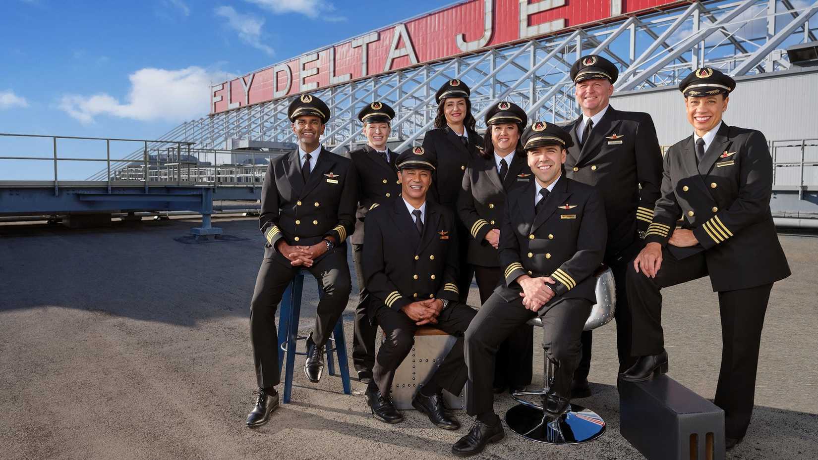 Group of eight Delta pilots gathered before historic Delta sign.