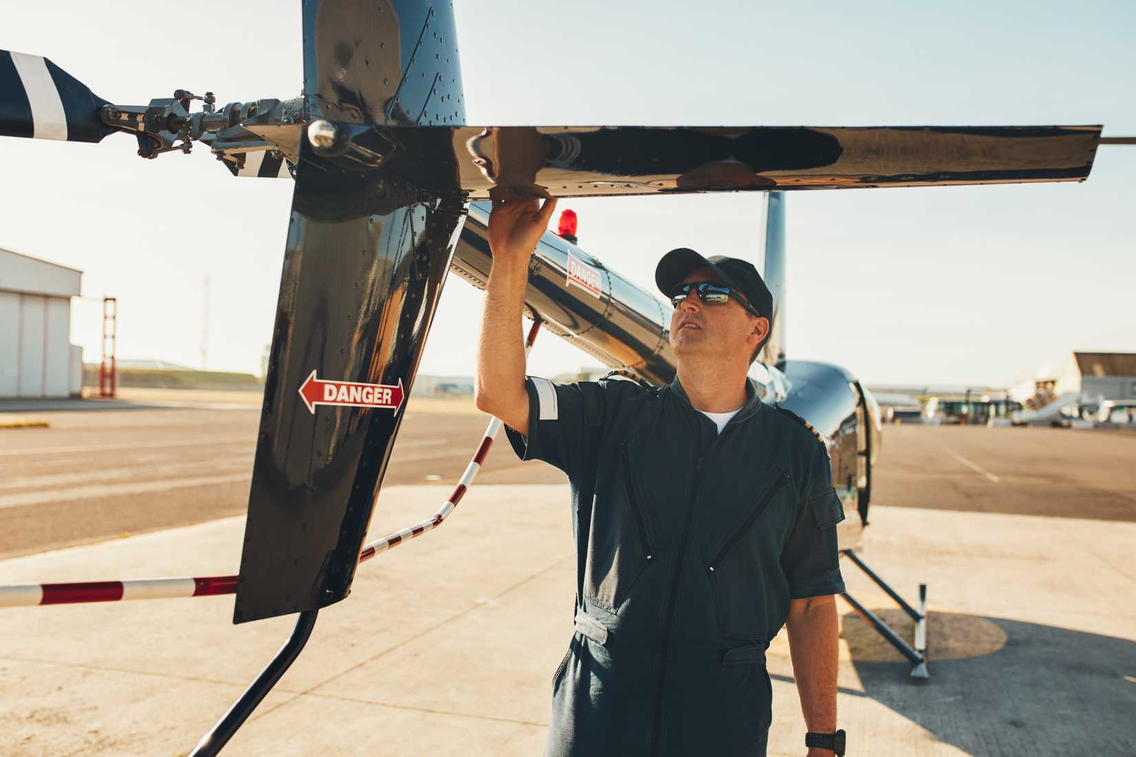 Male pilot in uniform examining helicopter tail wing. Pre flight inspection by pilot at the airport