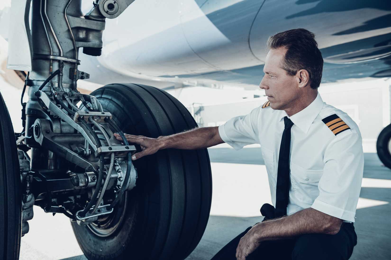 Checking the wheels. Confident male pilot in uniform examining an airplane wheels