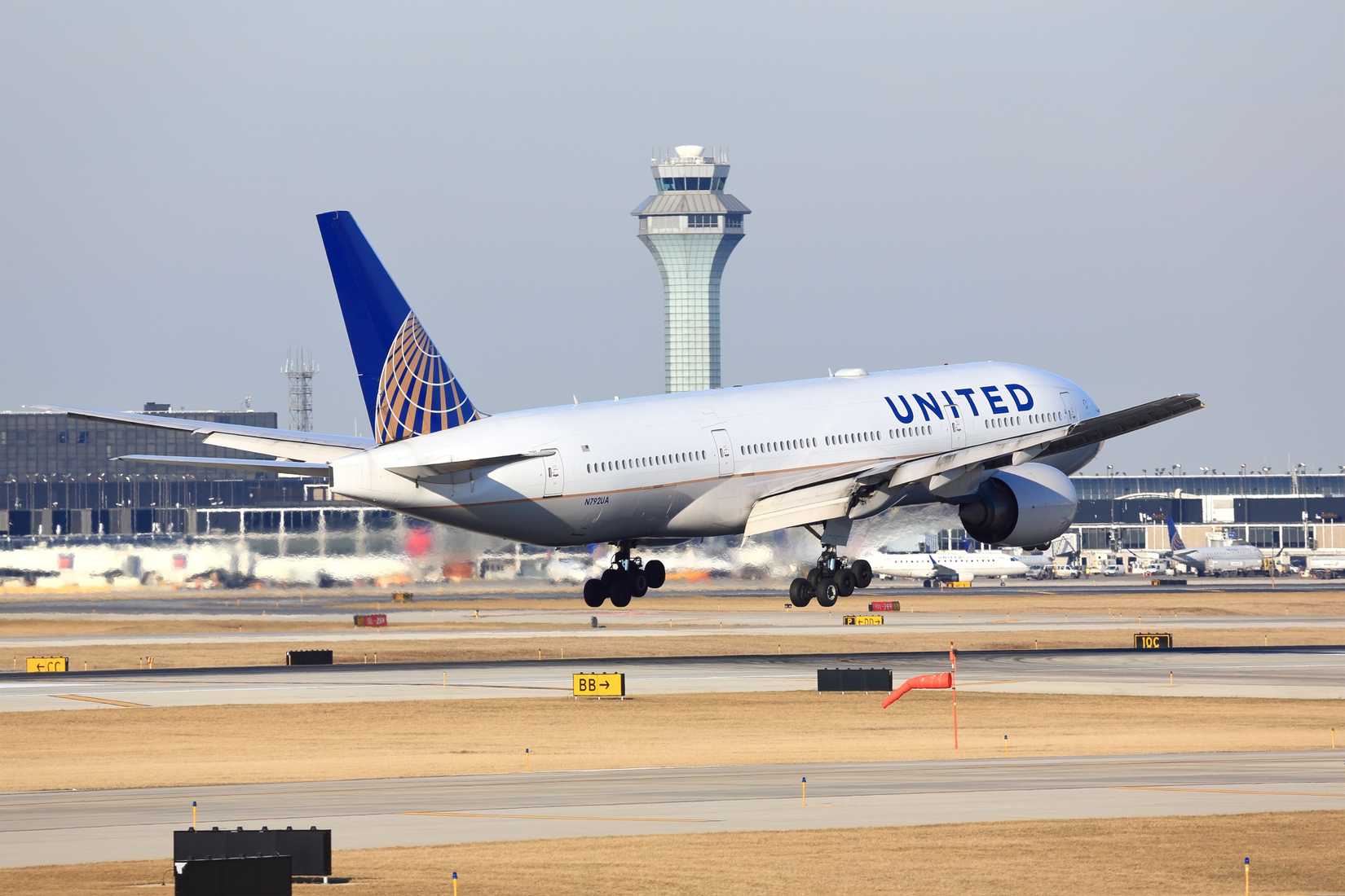 United Airlines Boeing 777-200 passenger jet airliner arriving for a landing at O'Hare International Airport in Chicago. Control tower in the background.