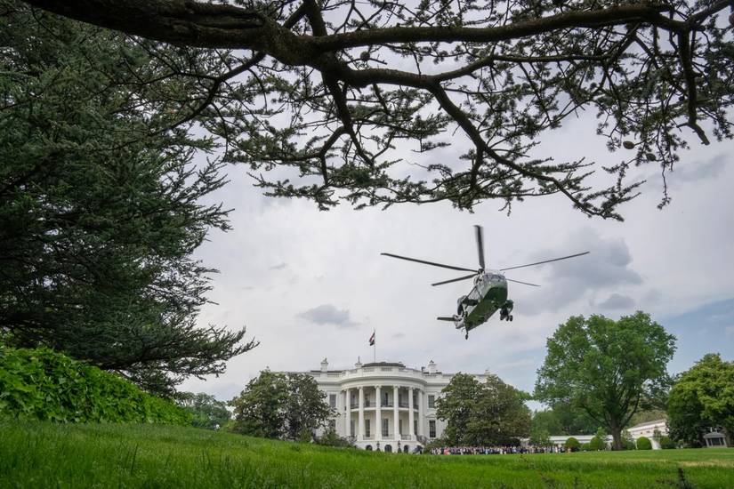 Wide shot of Marine One hovering over the White House south lawn