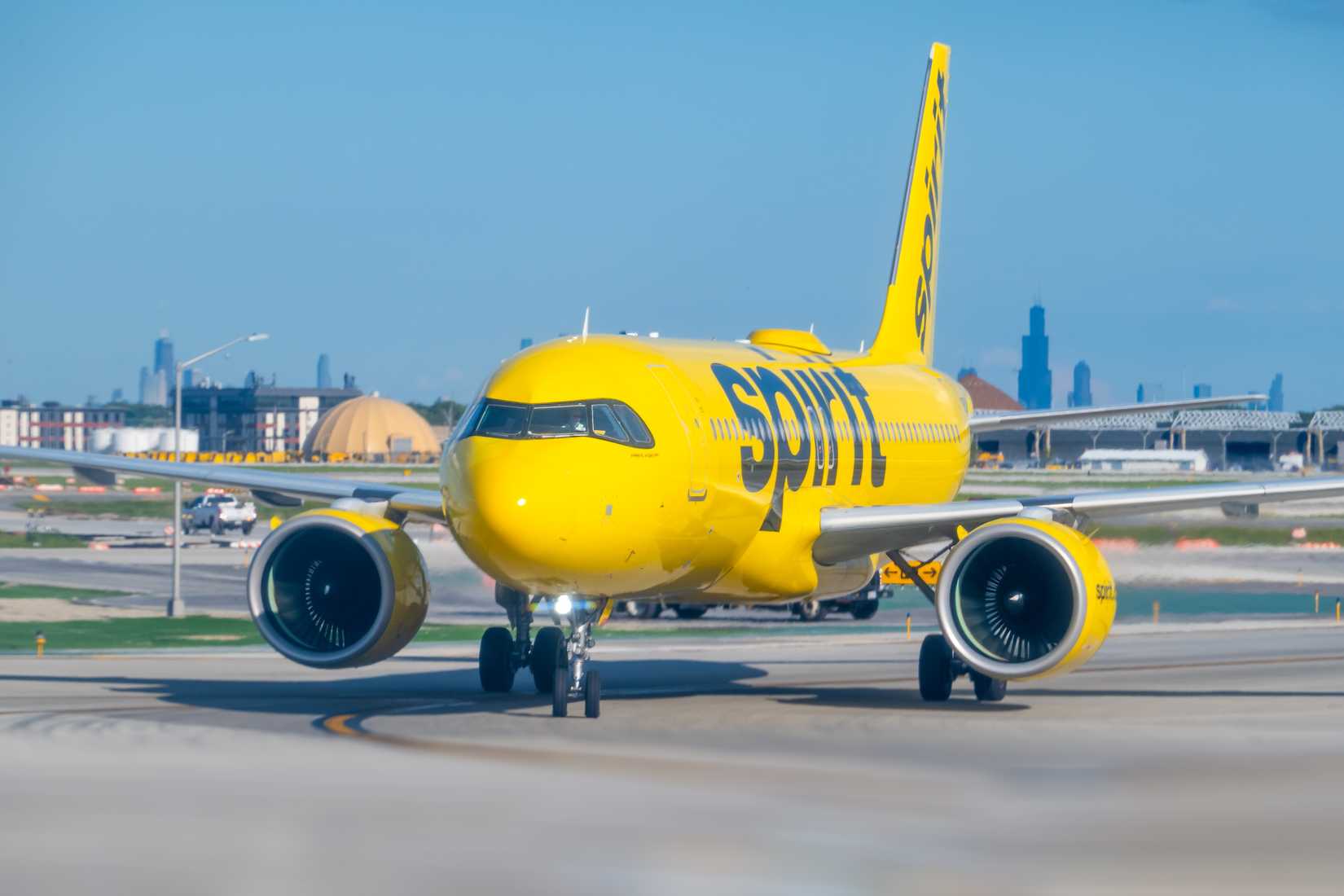A bright yellow Spirit Airlines airplane taxis on a sunny runway.