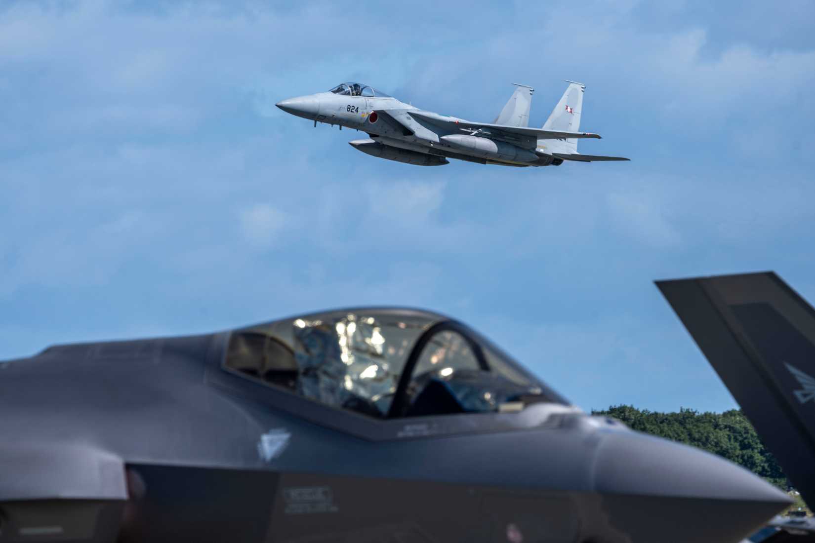 A Japan Air Self Defense Force (JASDF) F-15E Strike Eagle flies over a JASDF F-35 Lightning II.