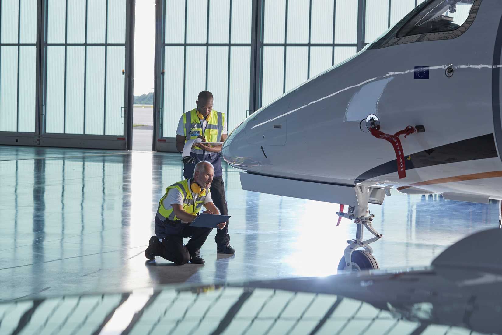 Ground crew workers examining corporate jet in airplane hangar