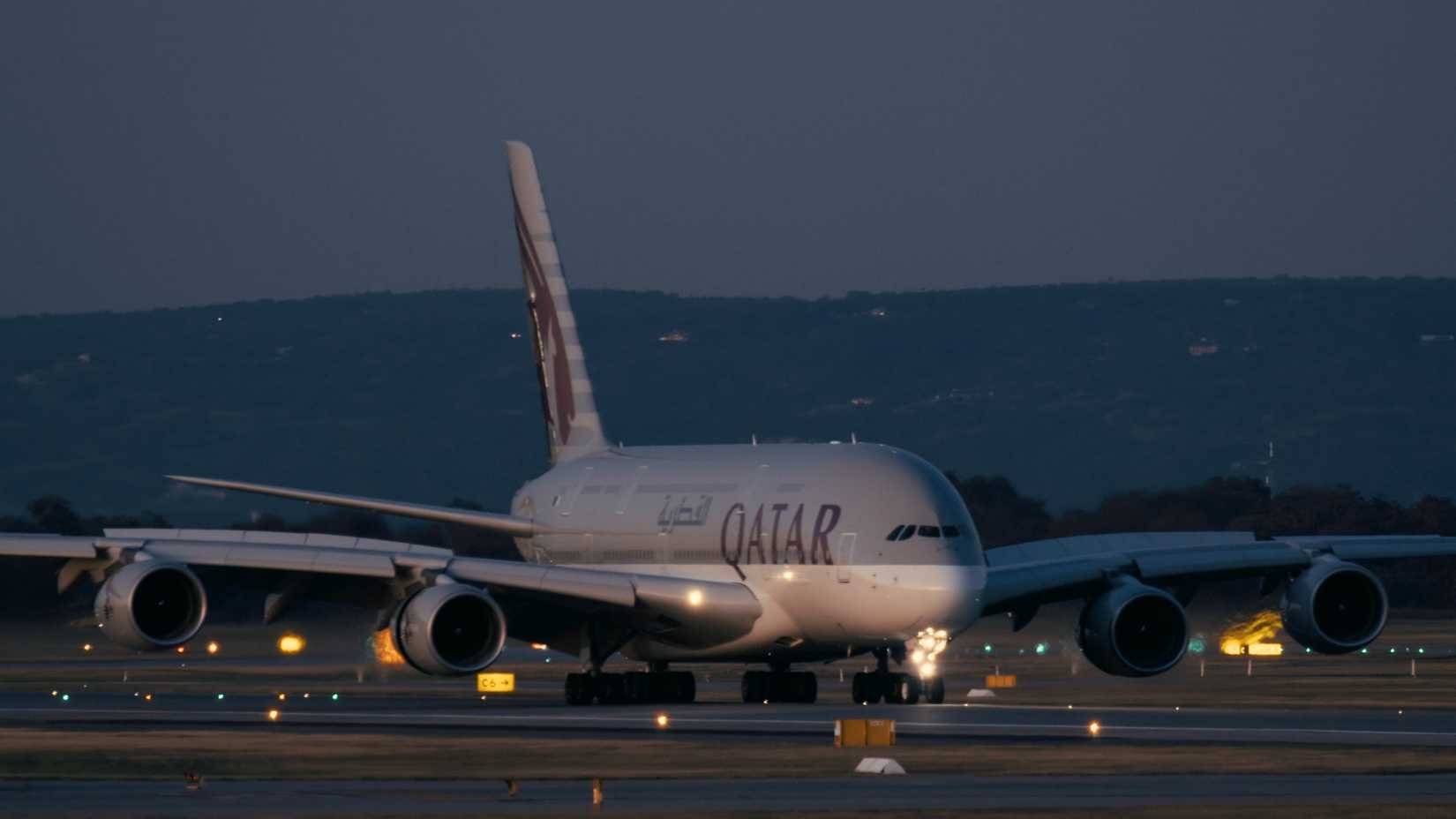 Large passenger airplane Airbus A380 of Qatar airlines prepares for night takeoff at the airport runway under a dimly lit sky.