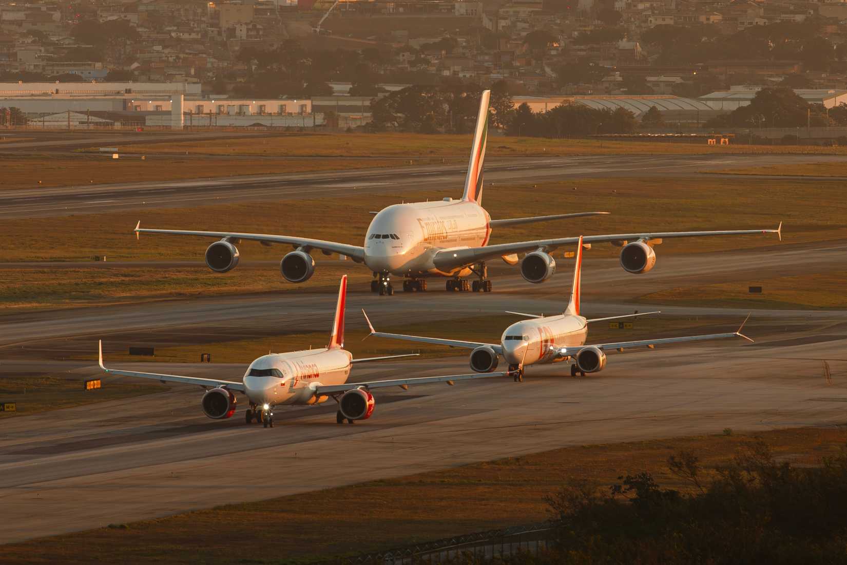 Line of aircraft including Airbus A320, Boeing 737-800, and Emirates A380 during sunset at Guarulhos Airport, São Paulo, Brazil,