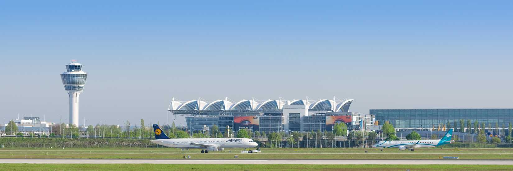 Panoramic view of Munich international airport with taxiing passenger airplanes and terminal.
