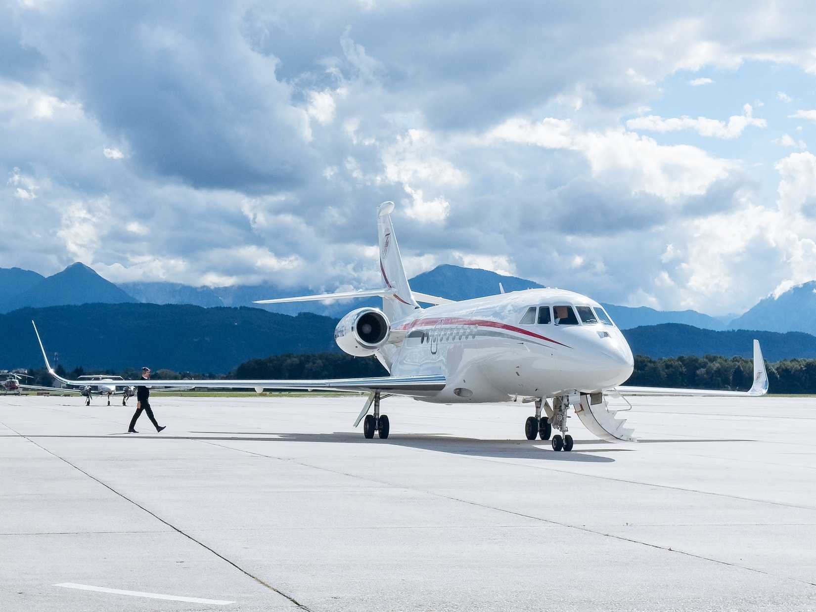 Private jet is parked on the runway with a pilot approaching.