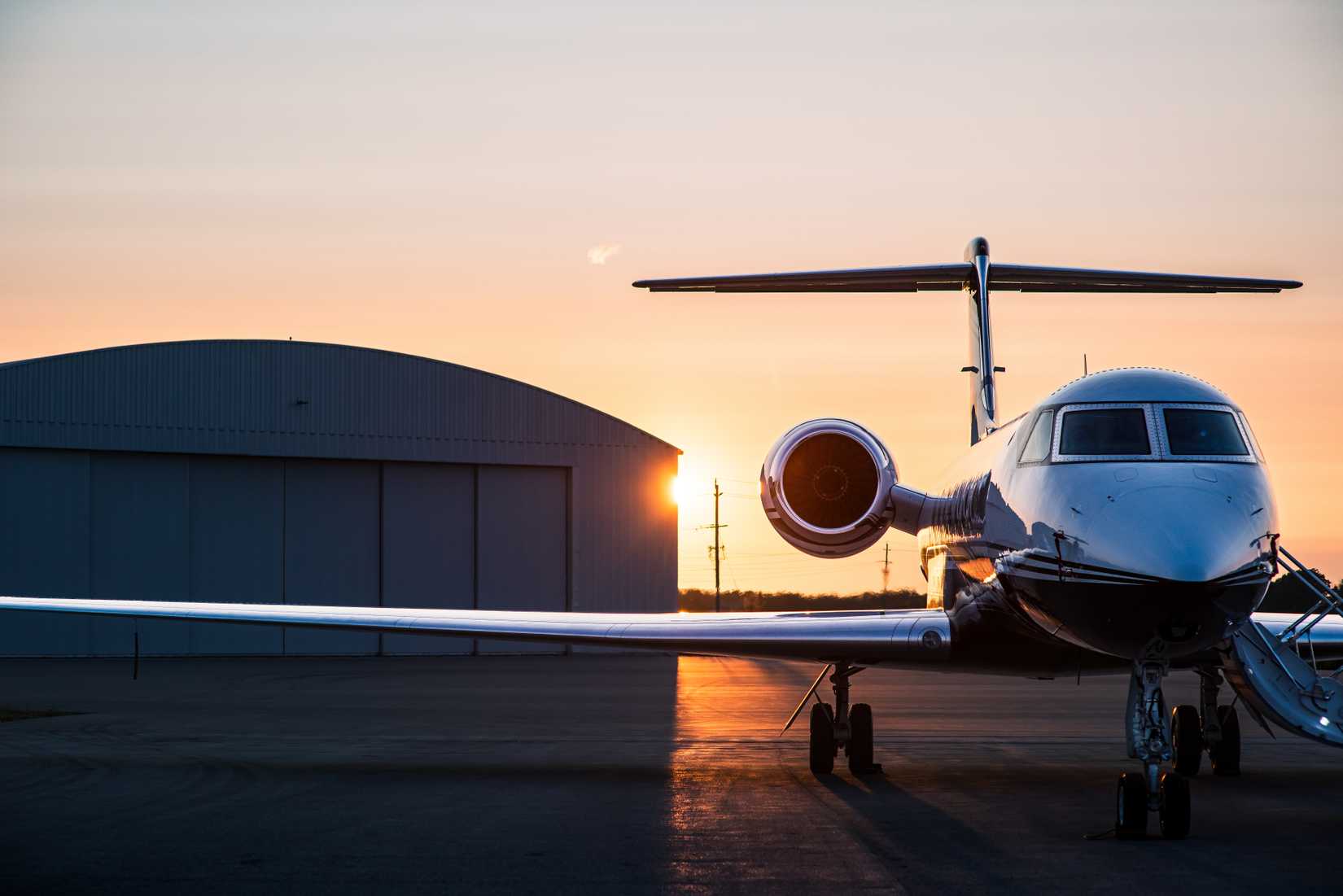 Private jet parked on tarmac at sunrise.