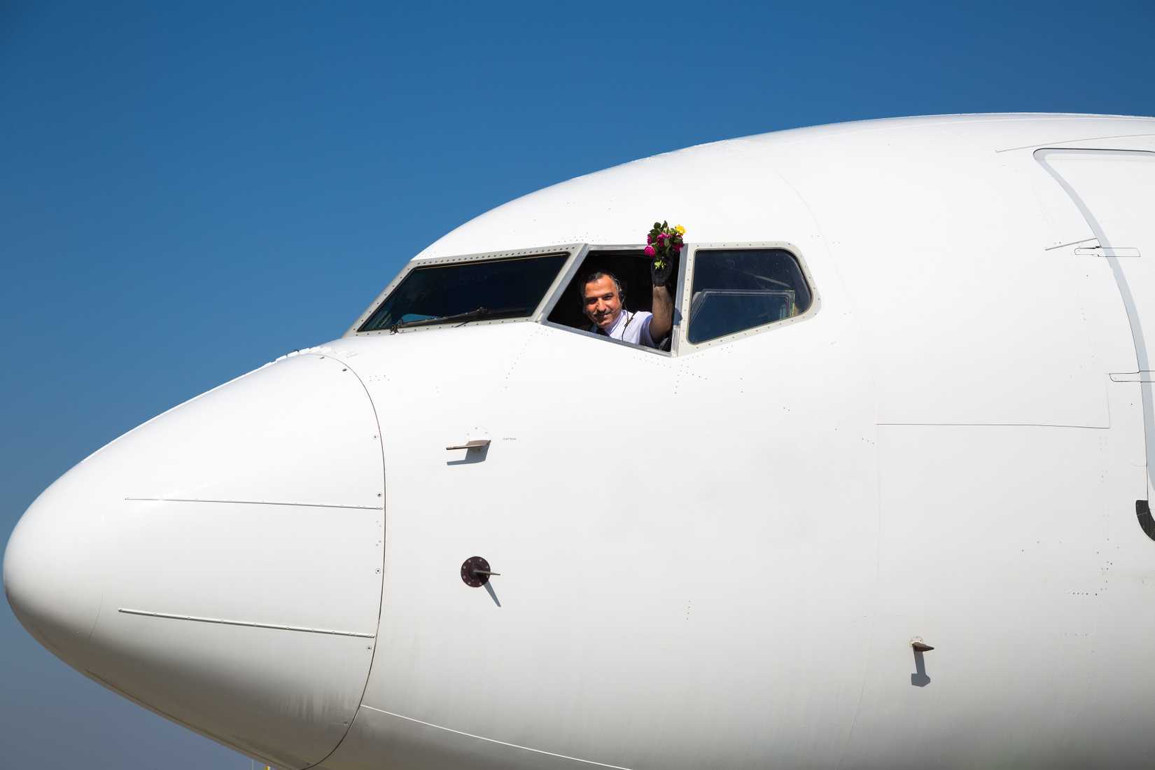 Pilot waving hand with a bouquet of flowers. Airline captain pilot. Airplane at the aiport
