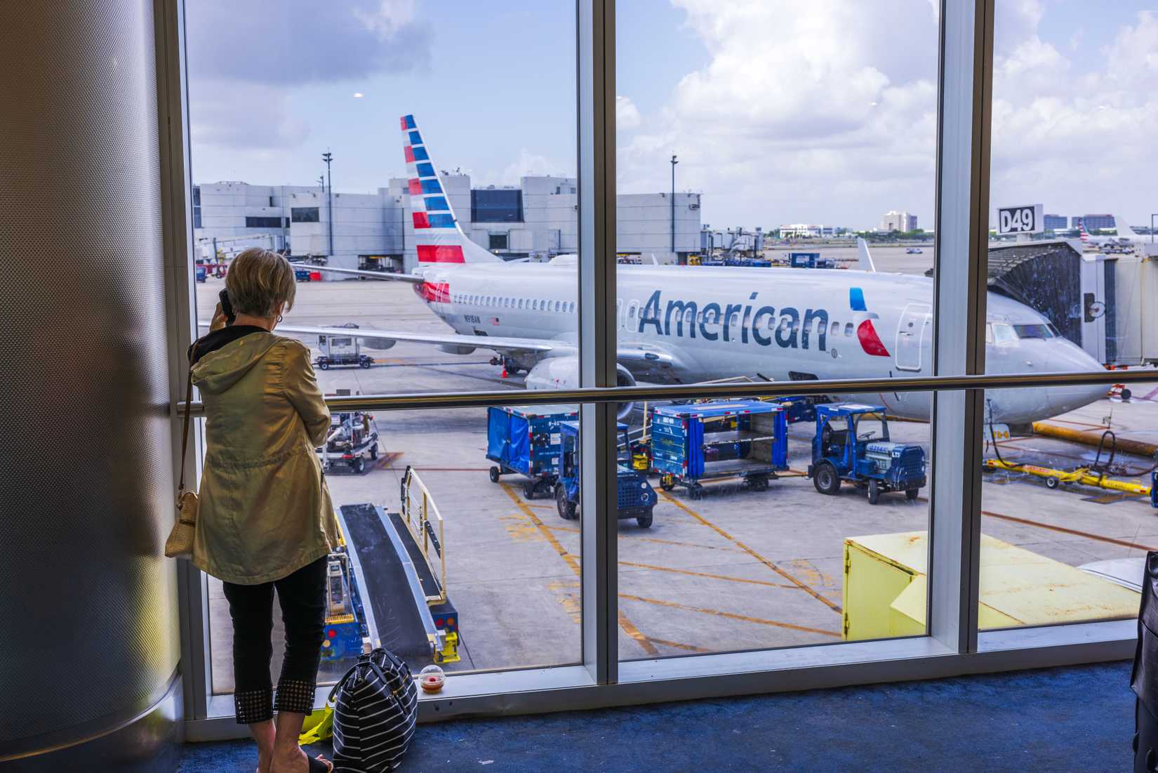 Close-up view of woman talking on mobile phone at the airport with American Airlines plane in the background. Miami