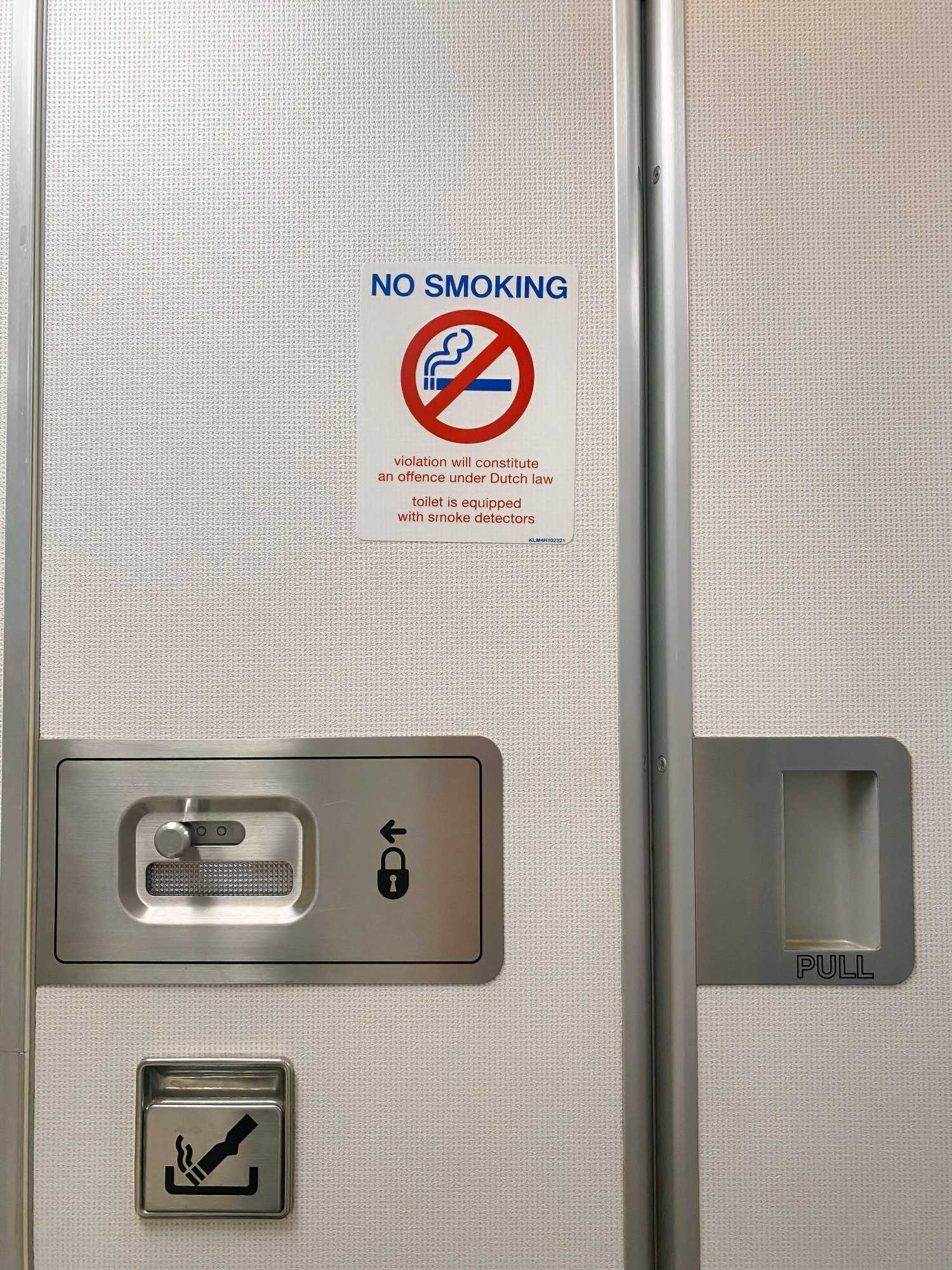 A lavatory door with no smoking signa and an ashtray on board of a KLM plane 