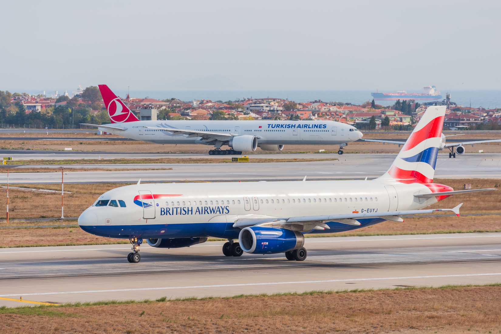 British Airways Airbus A320-232 (G-EUYJ) takes off from Istanbul Ataturk Airport with a Turkish Boeing 777 in the background
