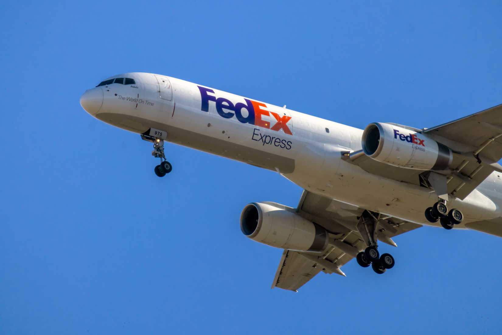 Um avião de carga da FedEx Express desce com o trem de pouso estendido contra um céu azul claro.