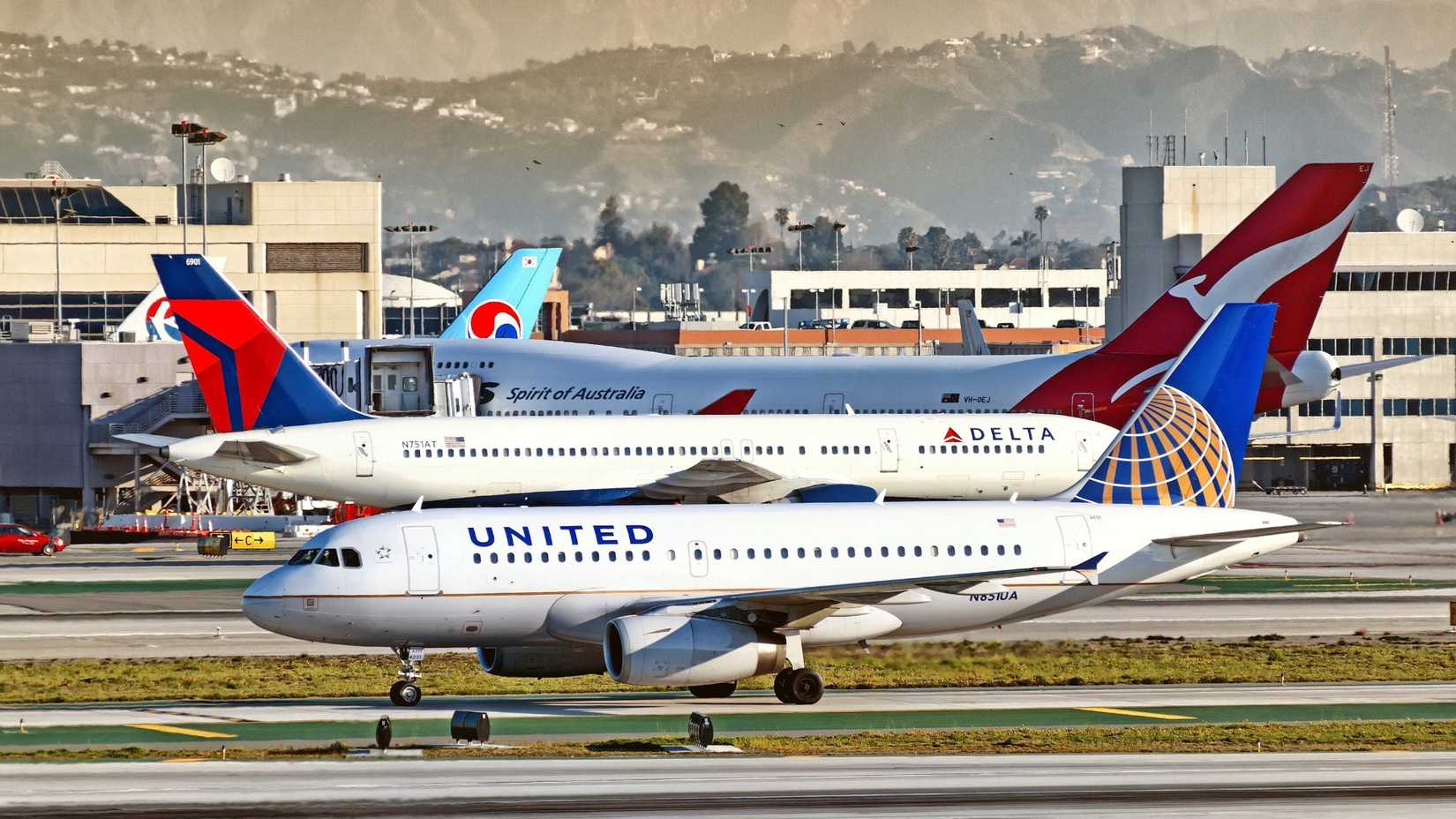 United and Delta Air Lines Aircraft taxiing on the runway; Qantas aircraft parked in the background