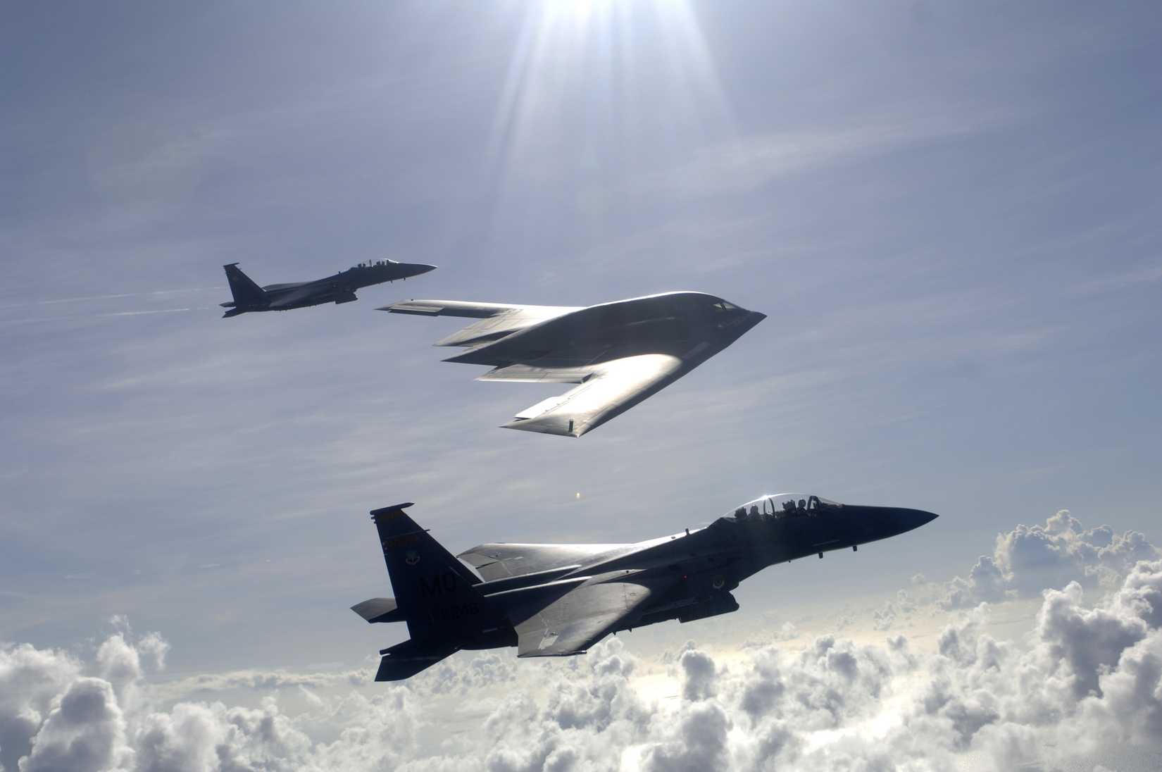 Air Force F-15E Strike Eagles and a B-2 Spirit bomber fly in formation over the Pacific Ocean