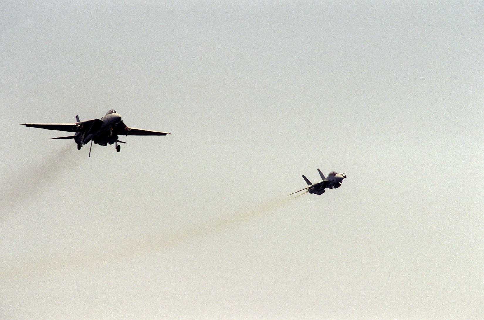 An F-14A Tomcat aircraft approaches for a landing aboard the aircraft carrier USS KITTY HAWK (CV-63) as another F-14A Tomcat flies past.