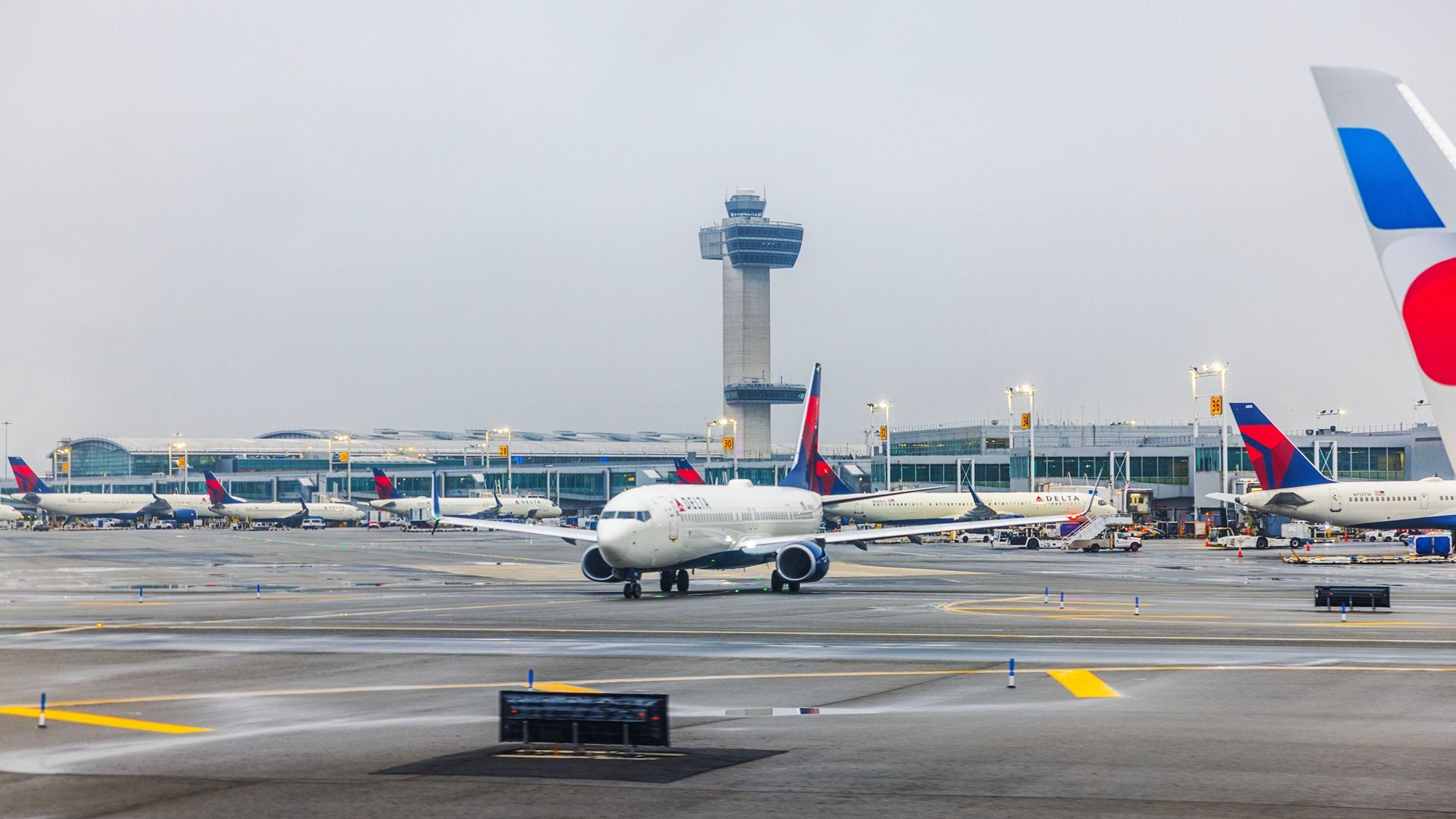 Delta Air Lines airplane taxiing on wet runway near terminal and control tower during cloudy weather. New York.