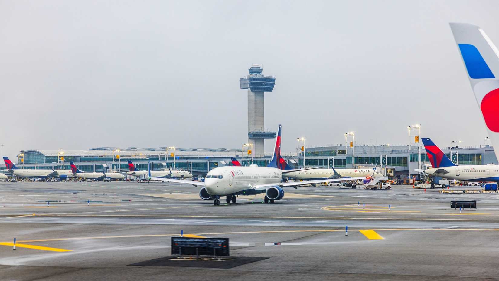 Delta Air Lines airplane taxiing on wet runway near terminal and control tower during cloudy weather. New York.