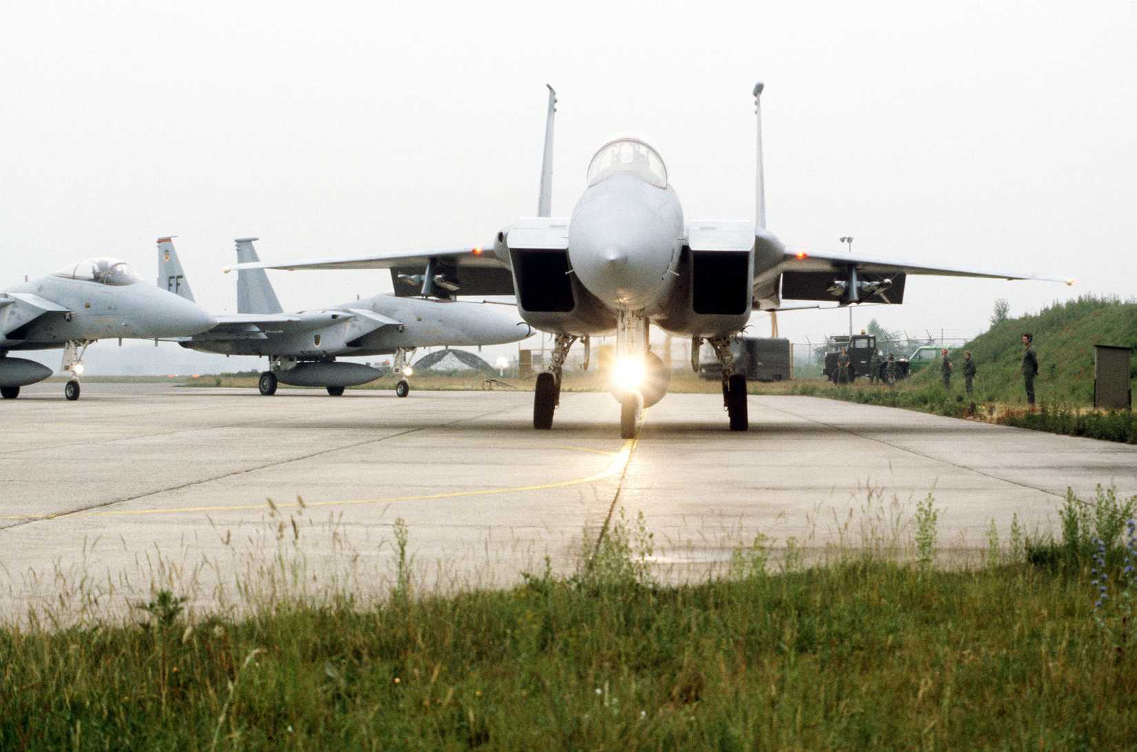Front view of an F-15A Eagle aircraft leaving a parking area as other F-15s follows.